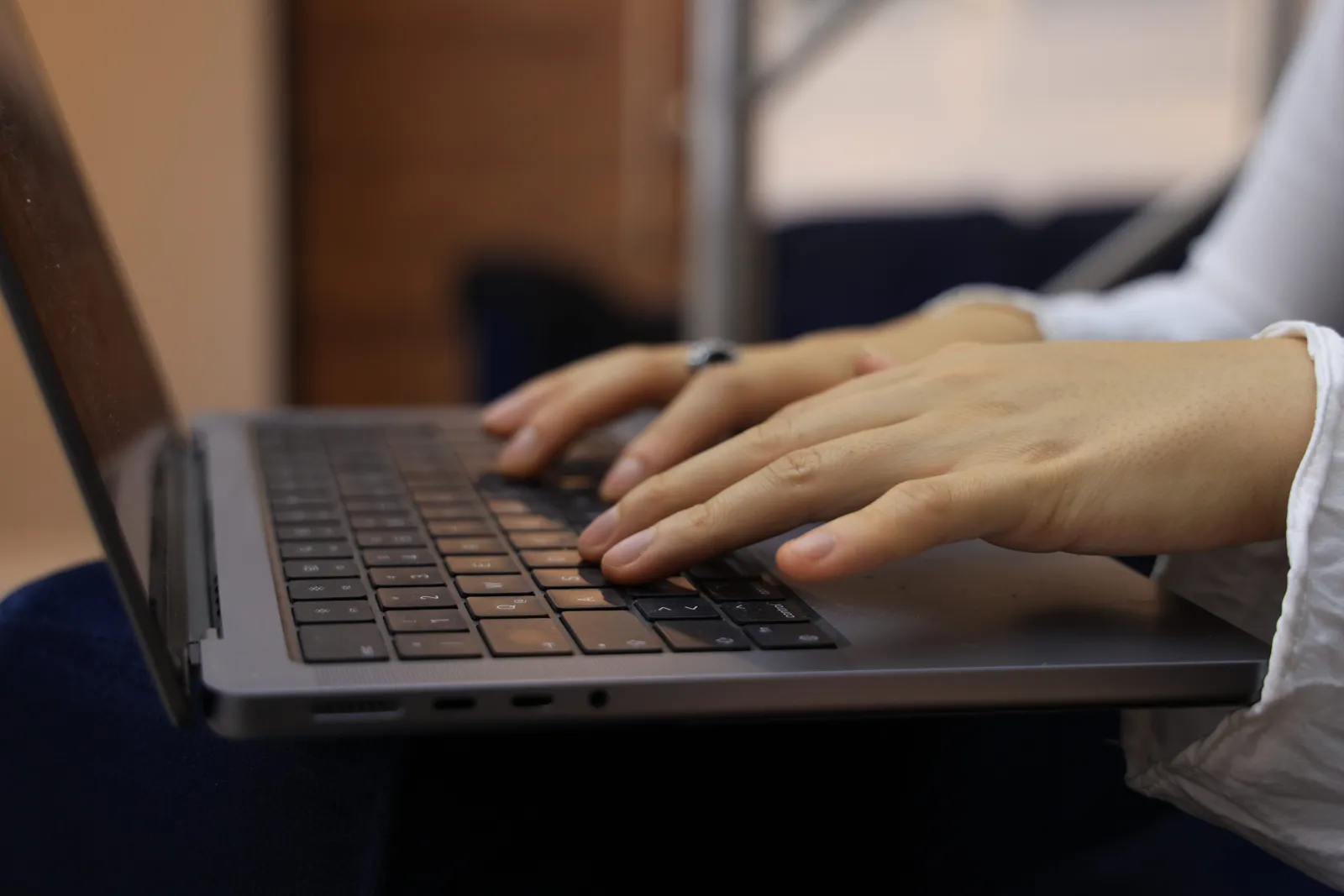Hands typing on a laptop keyboard, seen from the side