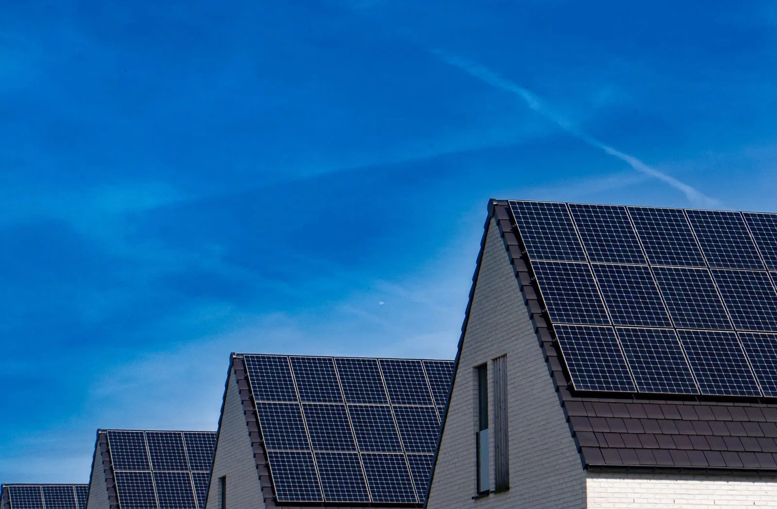 Rooftop solar panels on a row of houses under a deep blue sky