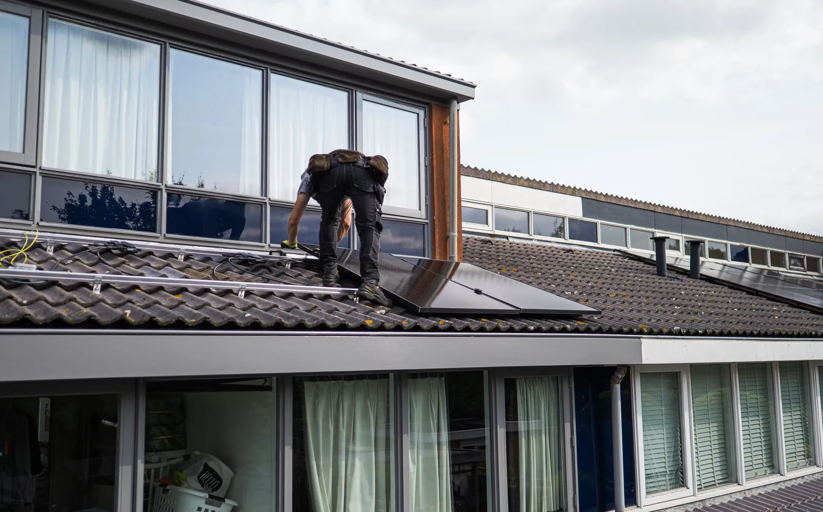 A technician installing solar panels on the tiled roof of a home