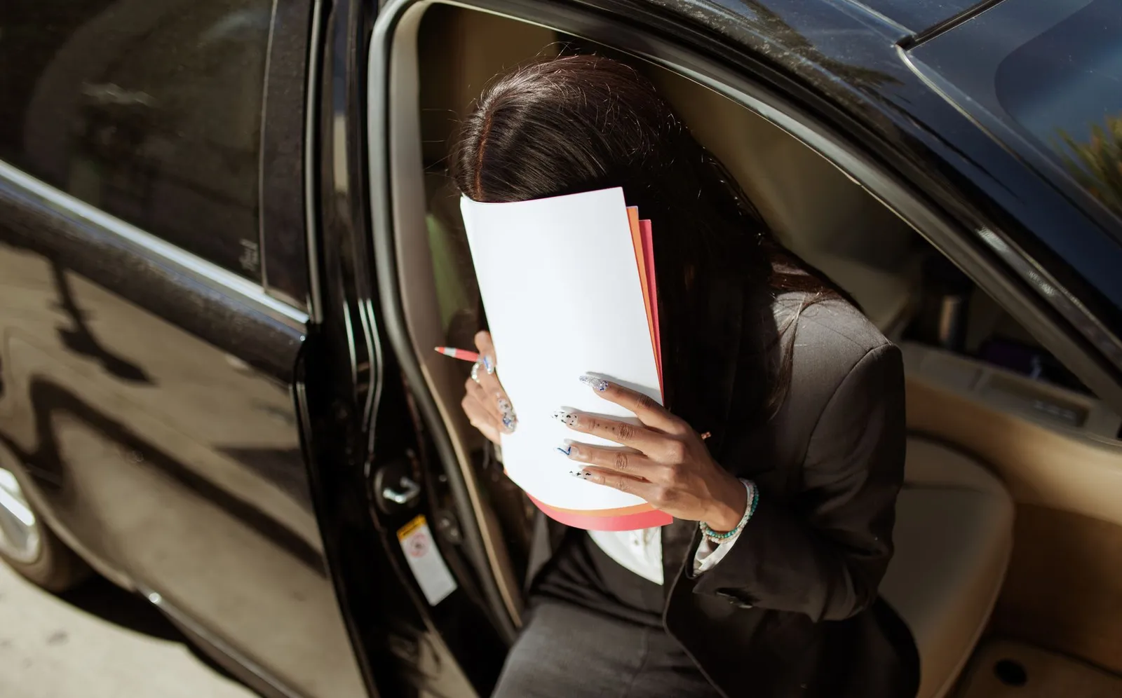Person sitting in a car doorway reading a stack of paperwork in daylight