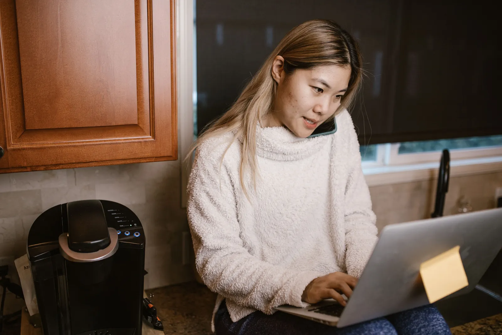 Woman at a kitchen table on a phone call with a laptop open in front of her