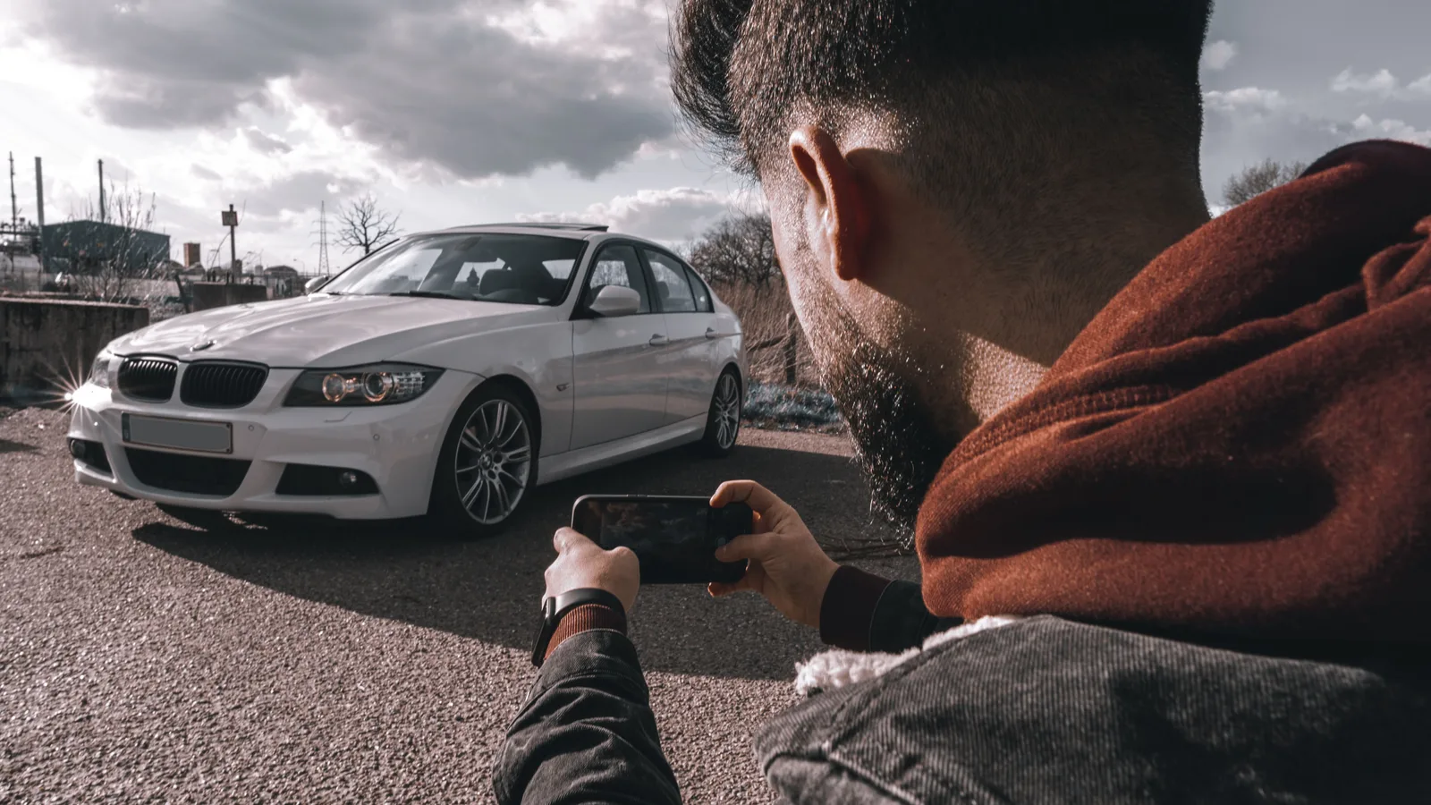 A person photographing a car with a smartphone outdoors