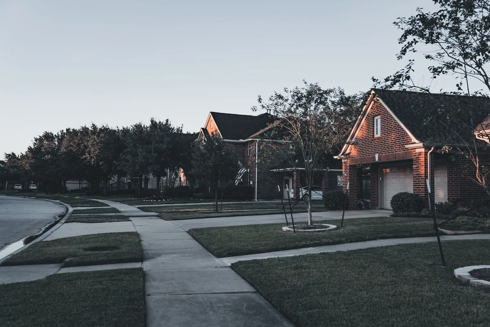 Brick suburban houses and green lawns along a curving sidewalk at dusk
