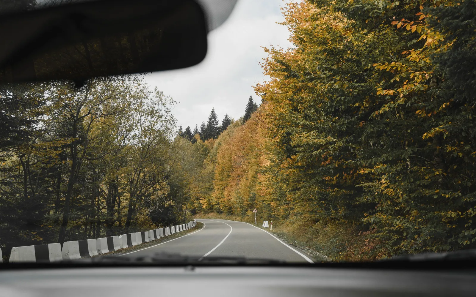 View through a car windshield of a two-lane road curving through autumn trees