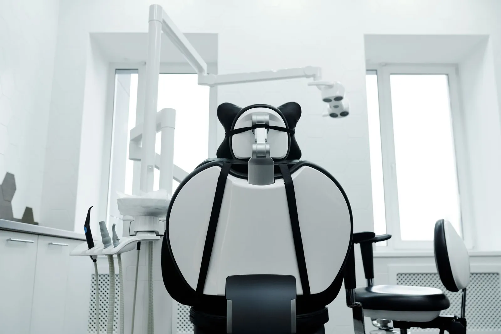 The back of an empty dental chair facing the overhead lamp in a bright, white treatment room