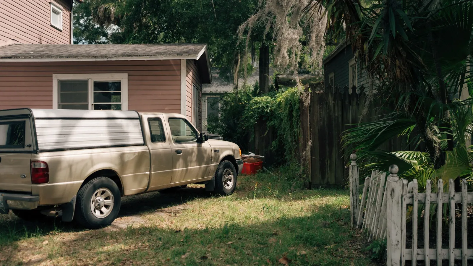 Older pickup truck parked on a grassy lot beside a small wooden house