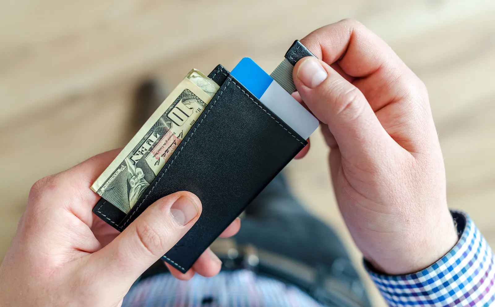 Hands pulling a card from a slim wallet that also holds a ten-dollar bill