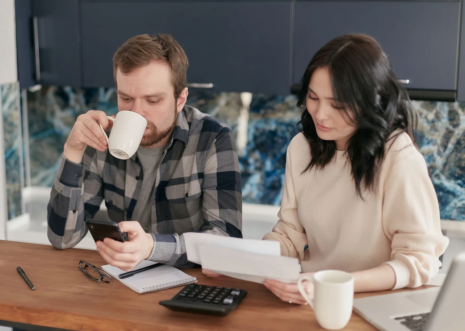 Couple at a kitchen counter going over bills with a phone, a notebook and a calculator