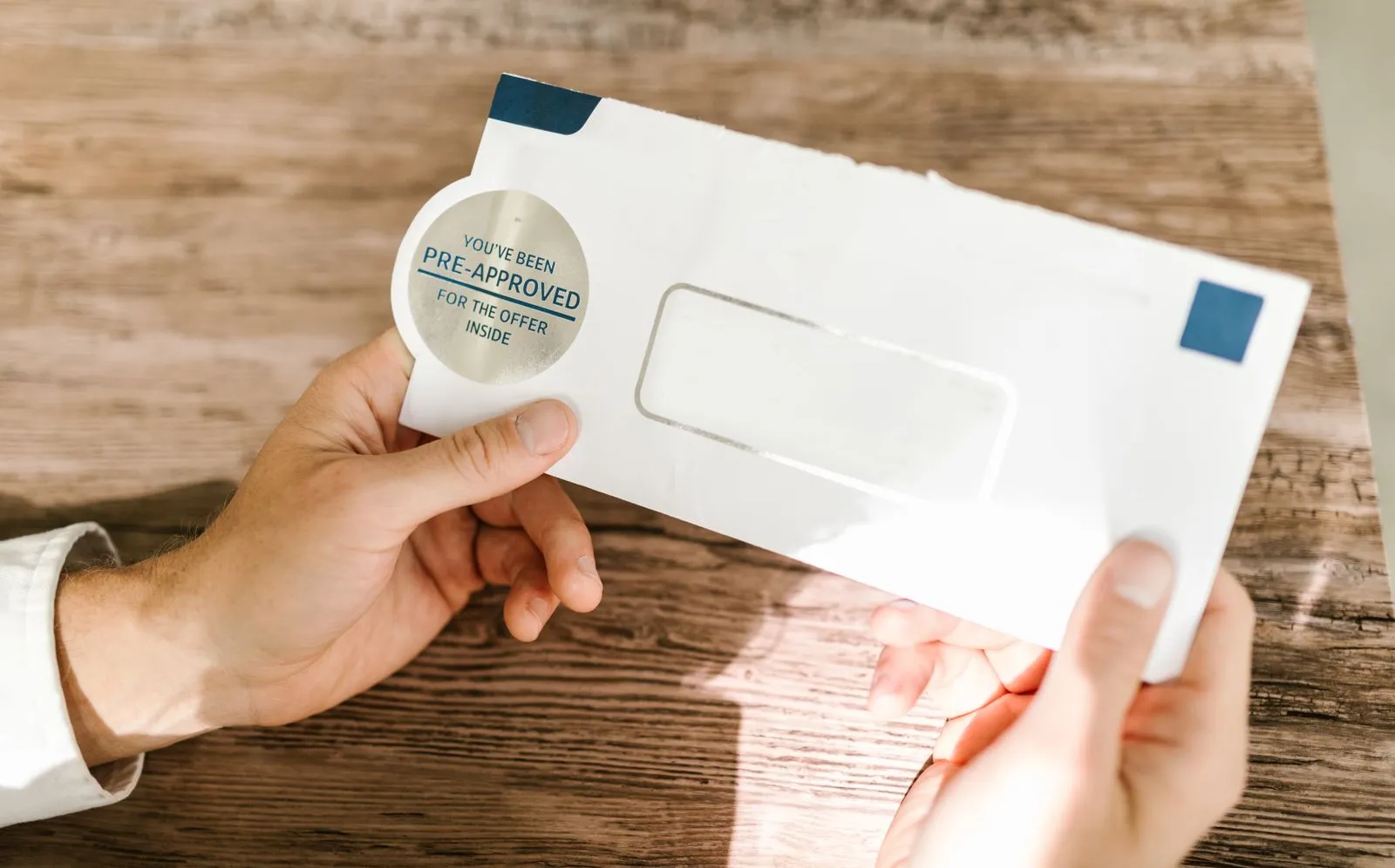 Hands holding a credit offer envelope on a wooden table