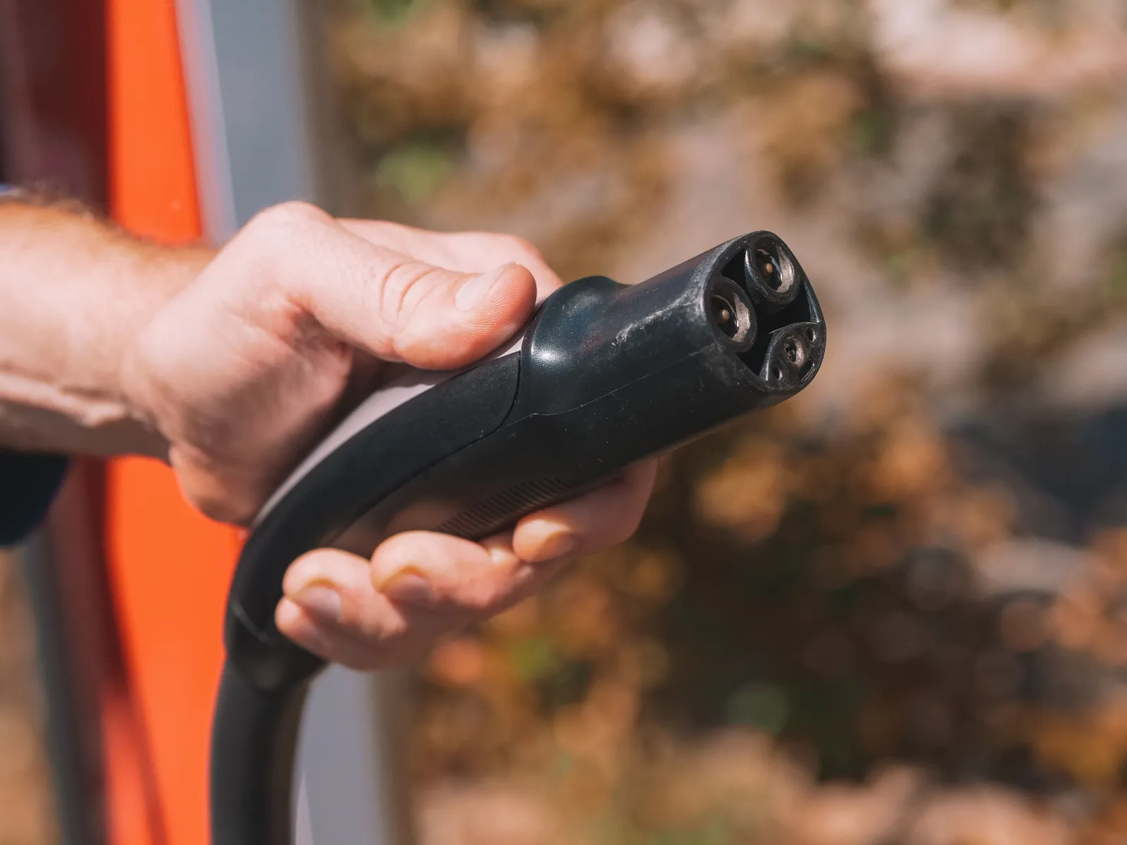 Close-up of a hand holding an electric vehicle charging connector beside a car