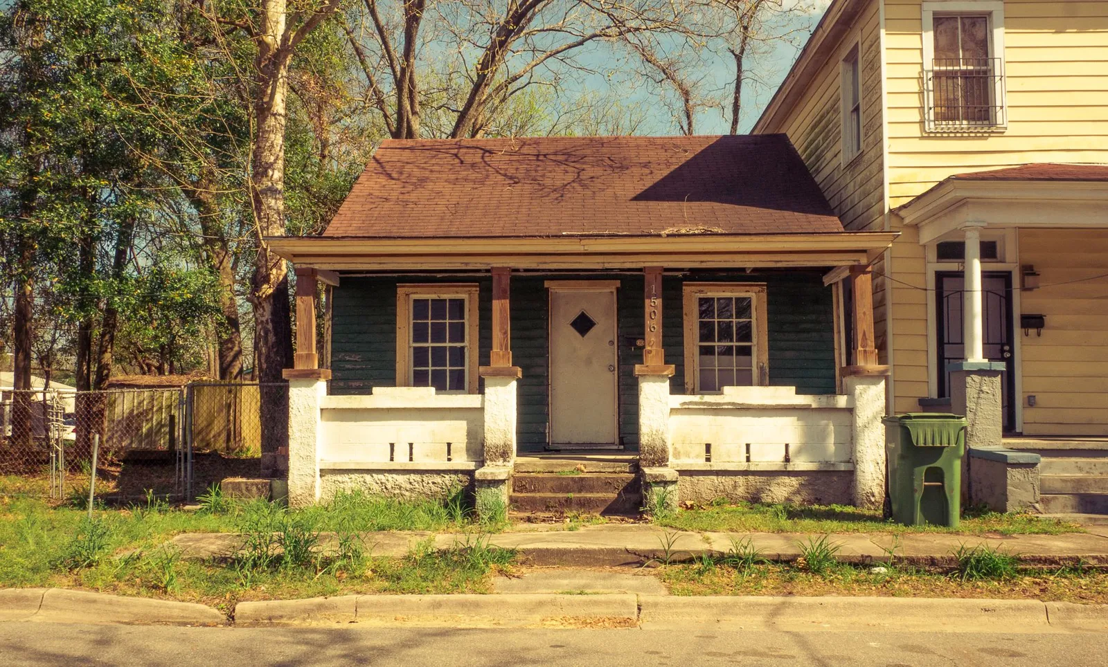 Small older green cottage with a worn roof, chipped porch masonry and weathered paint