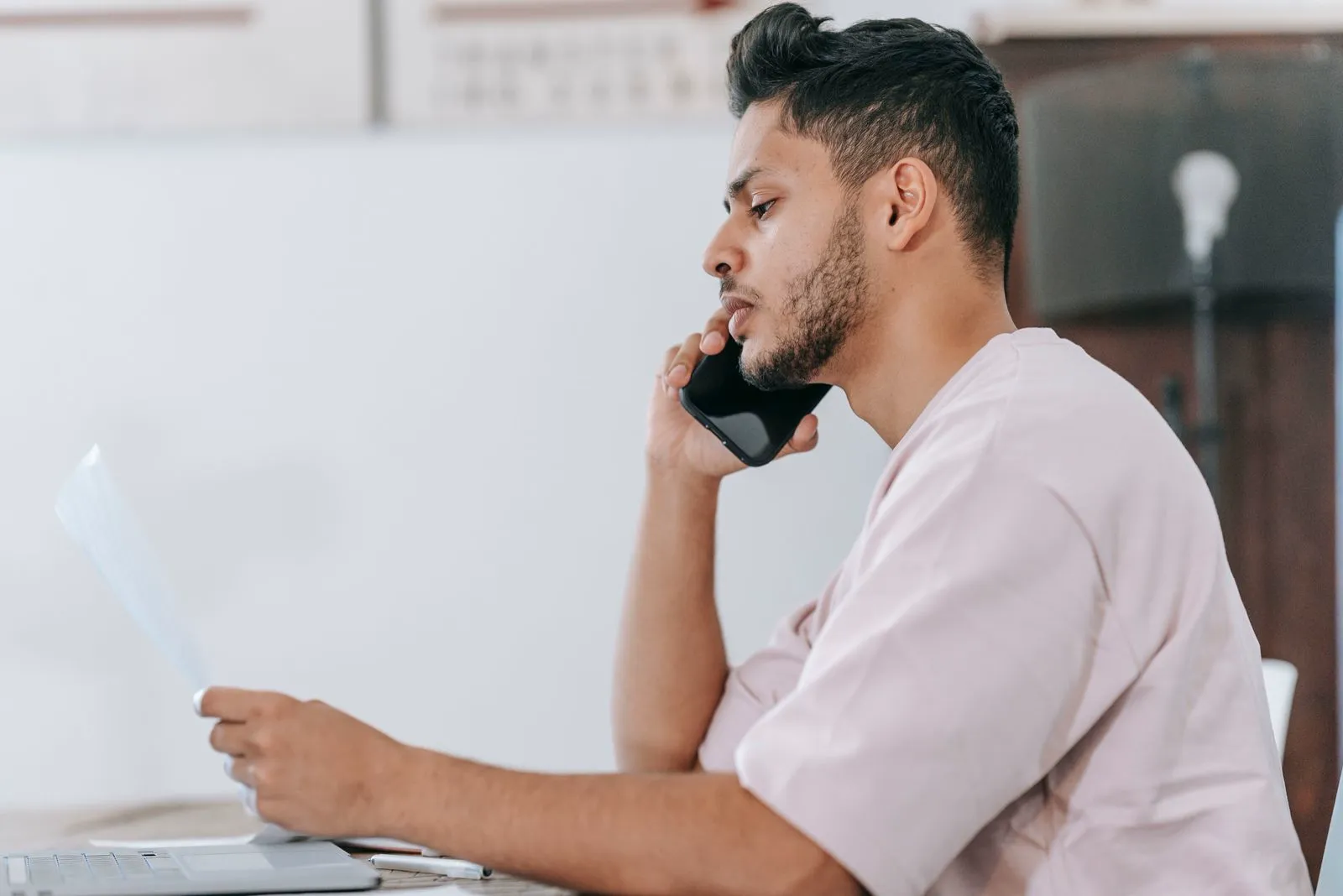 Man in a casual shirt reading a document while talking on a mobile phone