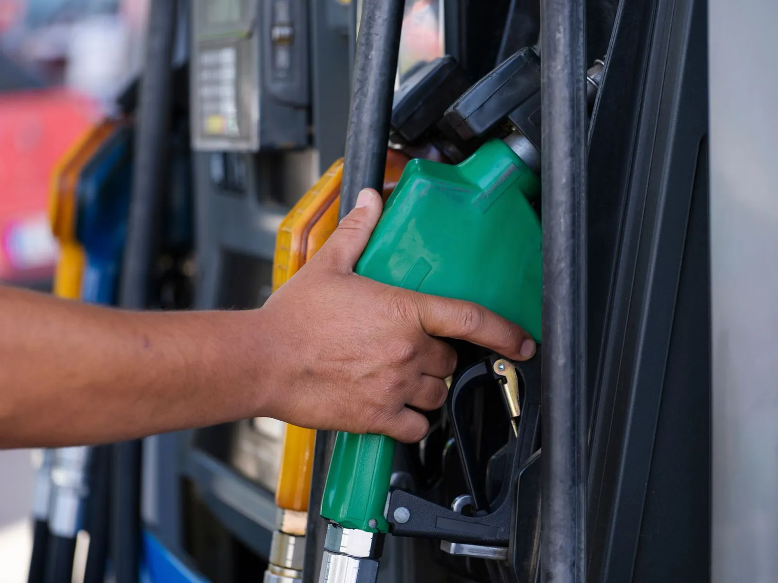 A hand pulling a fuel nozzle from a pump at a service station