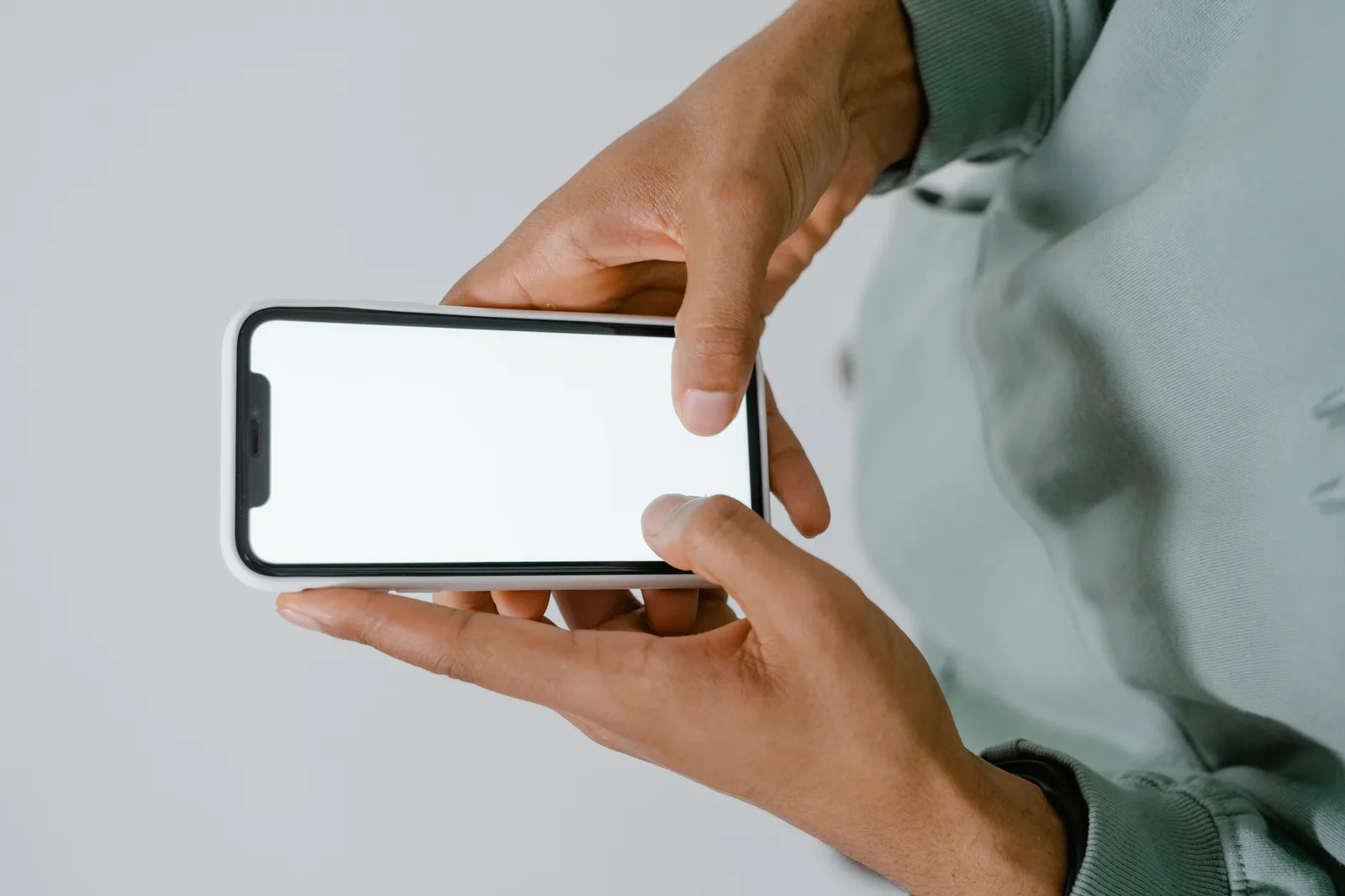 Two hands holding a smartphone with a blank white screen against a plain background