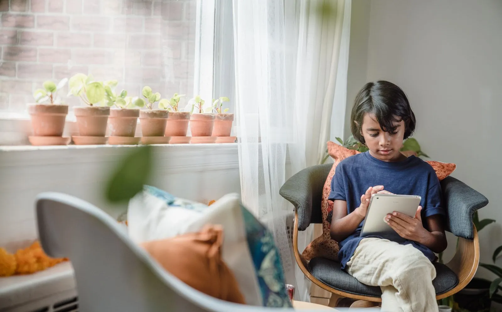 Young boy using a tablet while sitting in a room with plants nearby