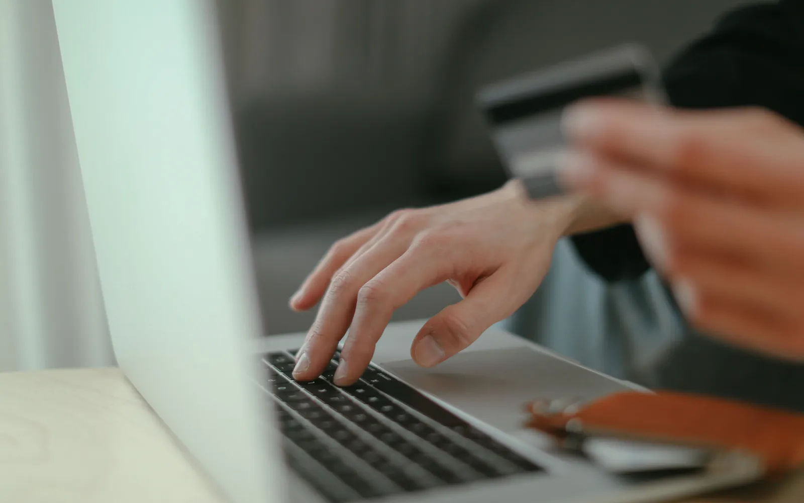 Close-up of a hand typing on a laptop keyboard while the other hand holds a payment card, slightly out of focus