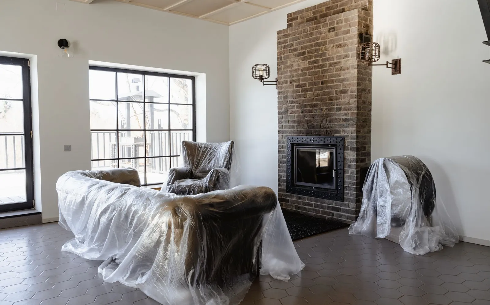 Living room with a sofa and armchair still wrapped in plastic beside a brick fireplace