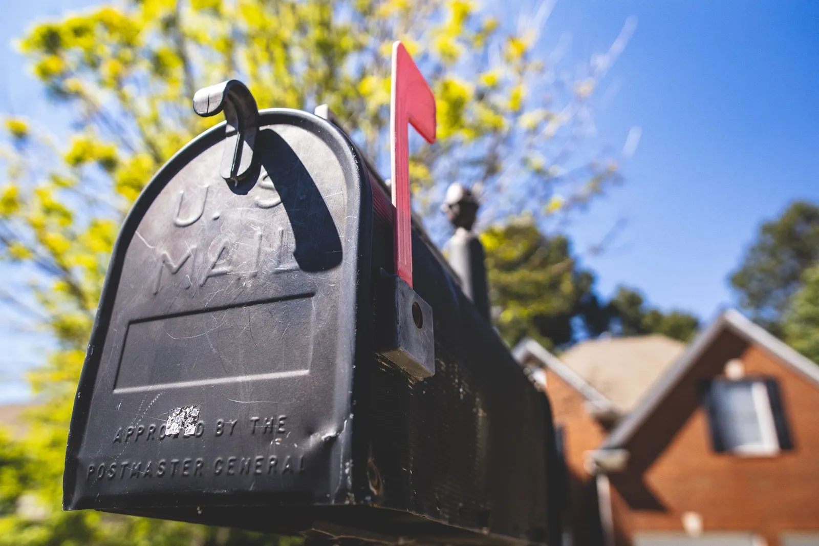 A black US mailbox with its red flag raised outside a suburban home