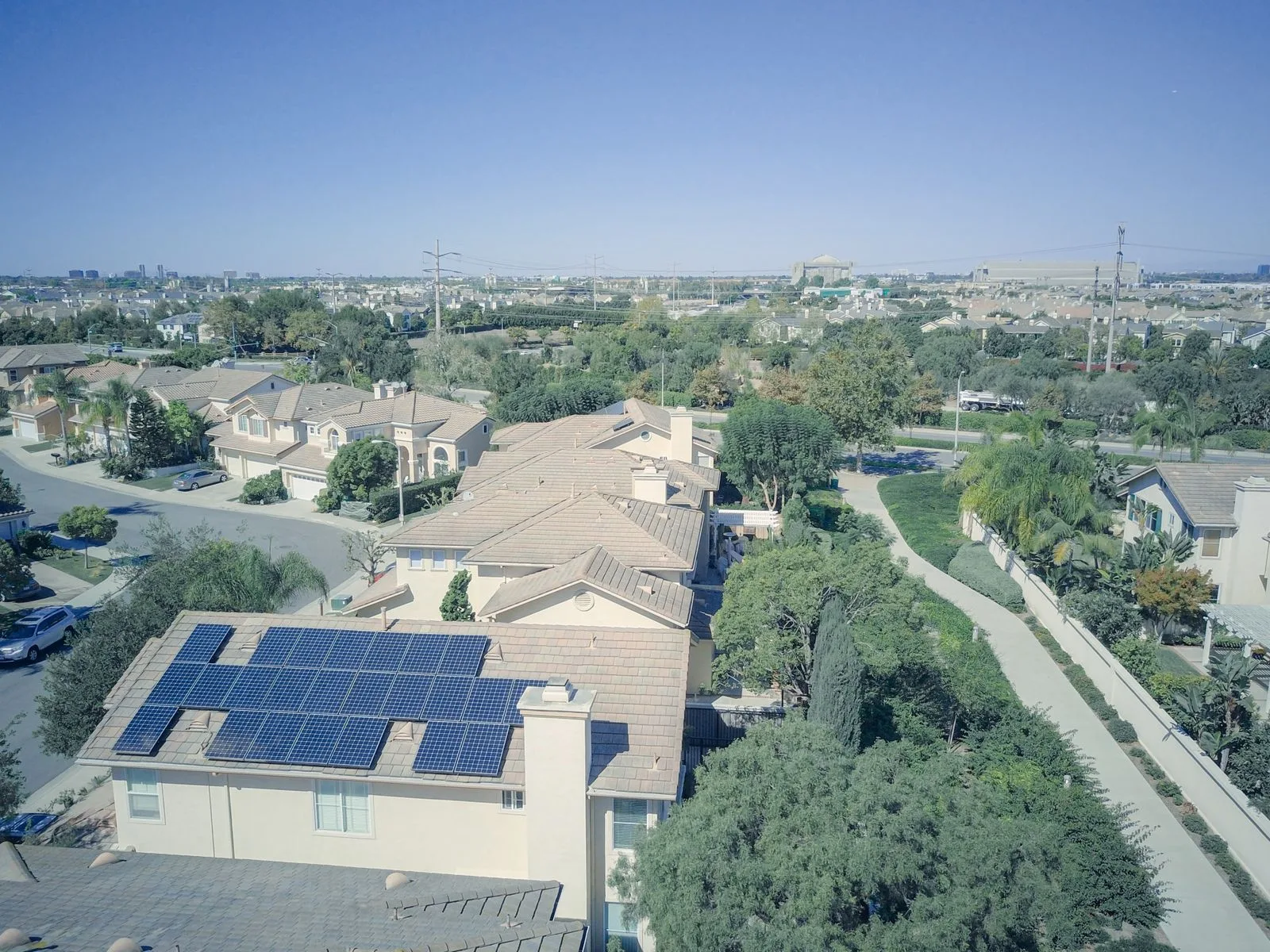 Aerial view of a suburban neighborhood with solar panels on a tile rooftop in the foreground