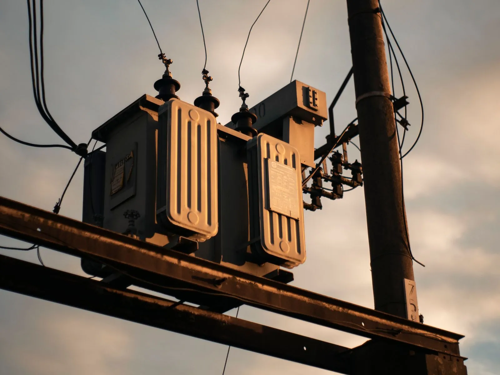 A pole-mounted electrical transformer and power lines at sunset