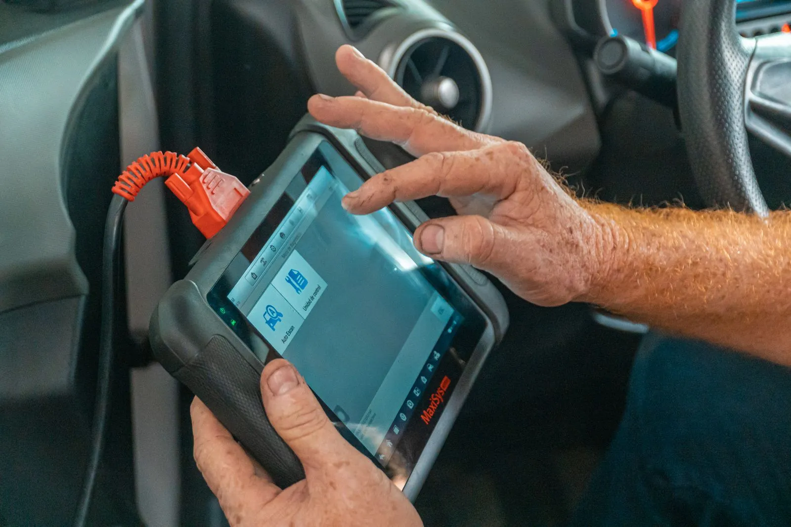 Technician holding a diagnostic scan tool plugged into a car's dashboard port