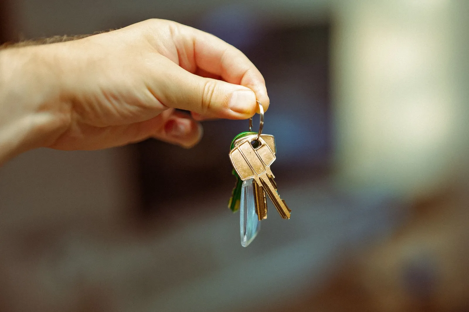 A hand holding up a ring of house keys against a blurred living room