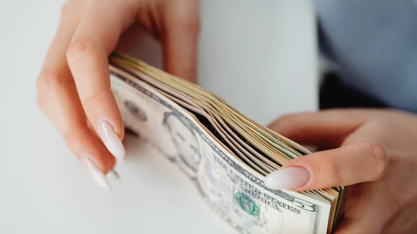 Two hands fanning through a thick stack of US dollar bills on a white table