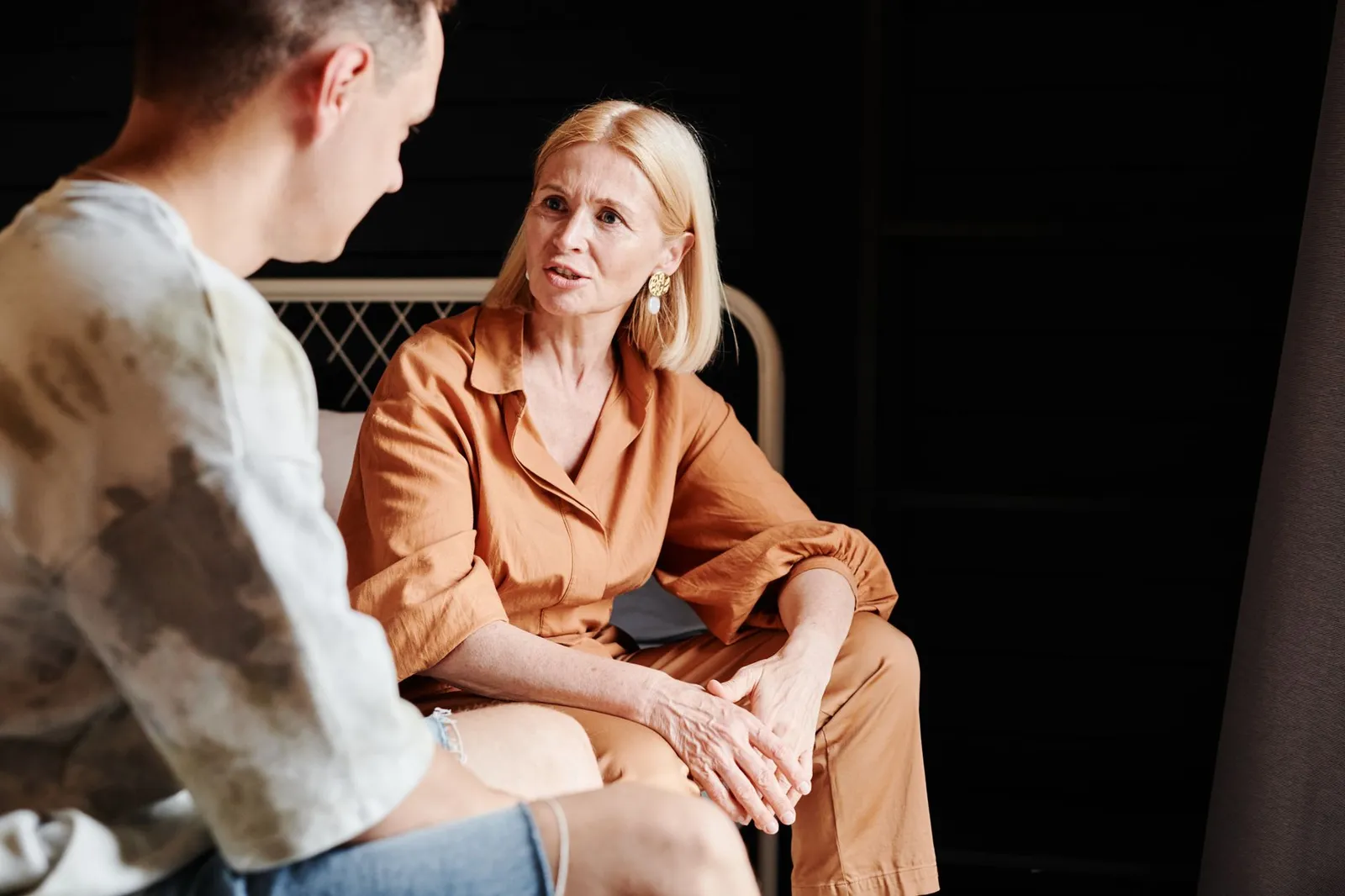An older woman in an orange shirt talking seriously with a younger man seated across from her