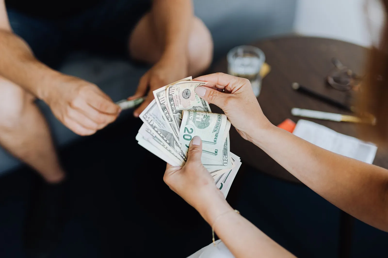 Hands counting out a fan of twenty and ten dollar bills while another person reaches across a table