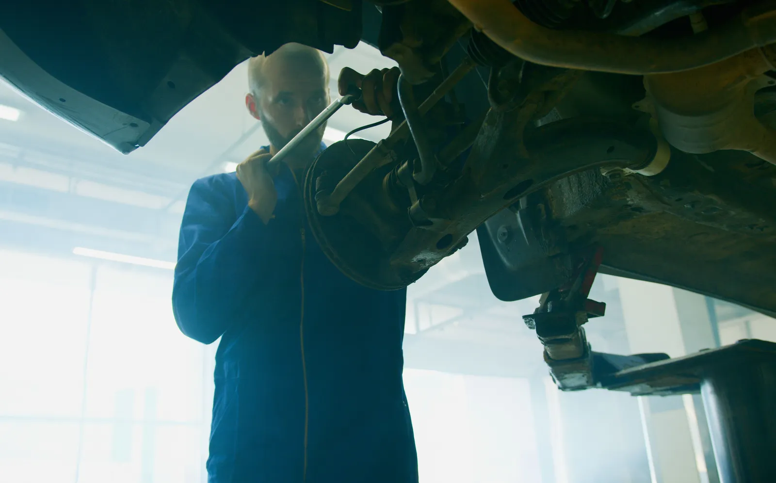 A mechanic in blue coveralls working underneath a car raised on a shop lift