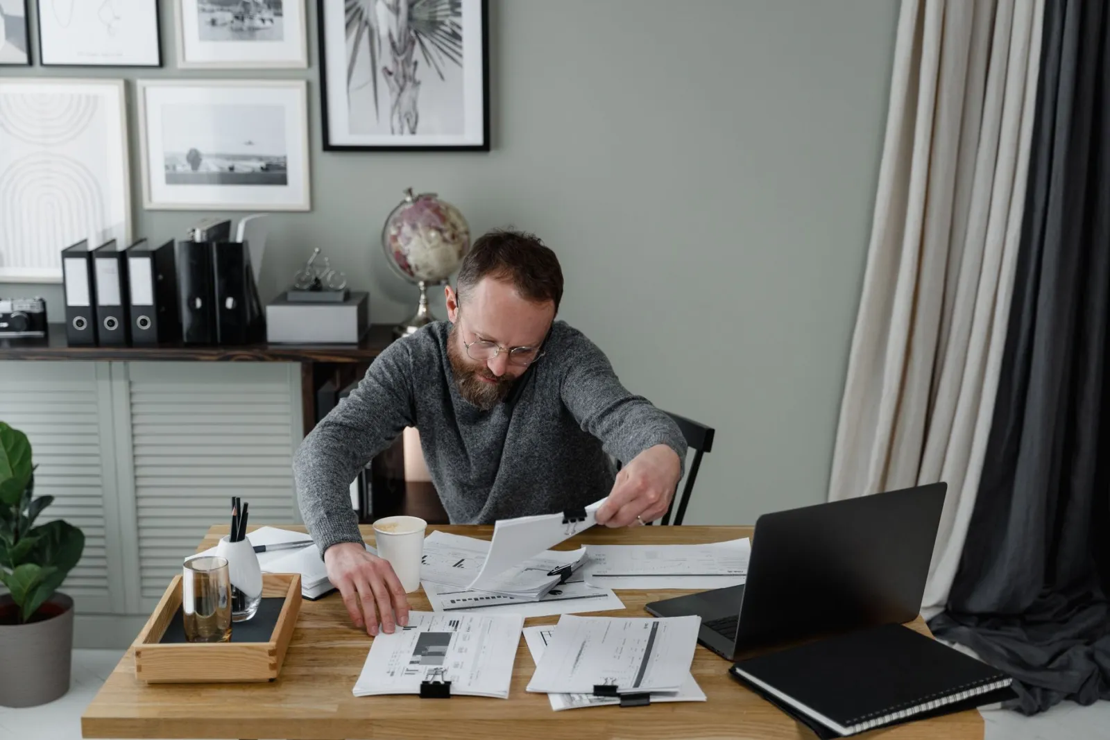 A person reviewing documents at an office desk with a laptop and a cup of coffee