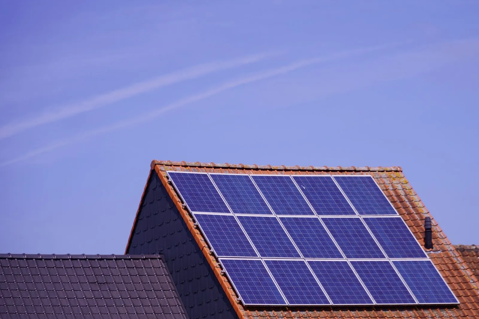 Solar panels mounted on the red tile roof of a house against a clear blue sky