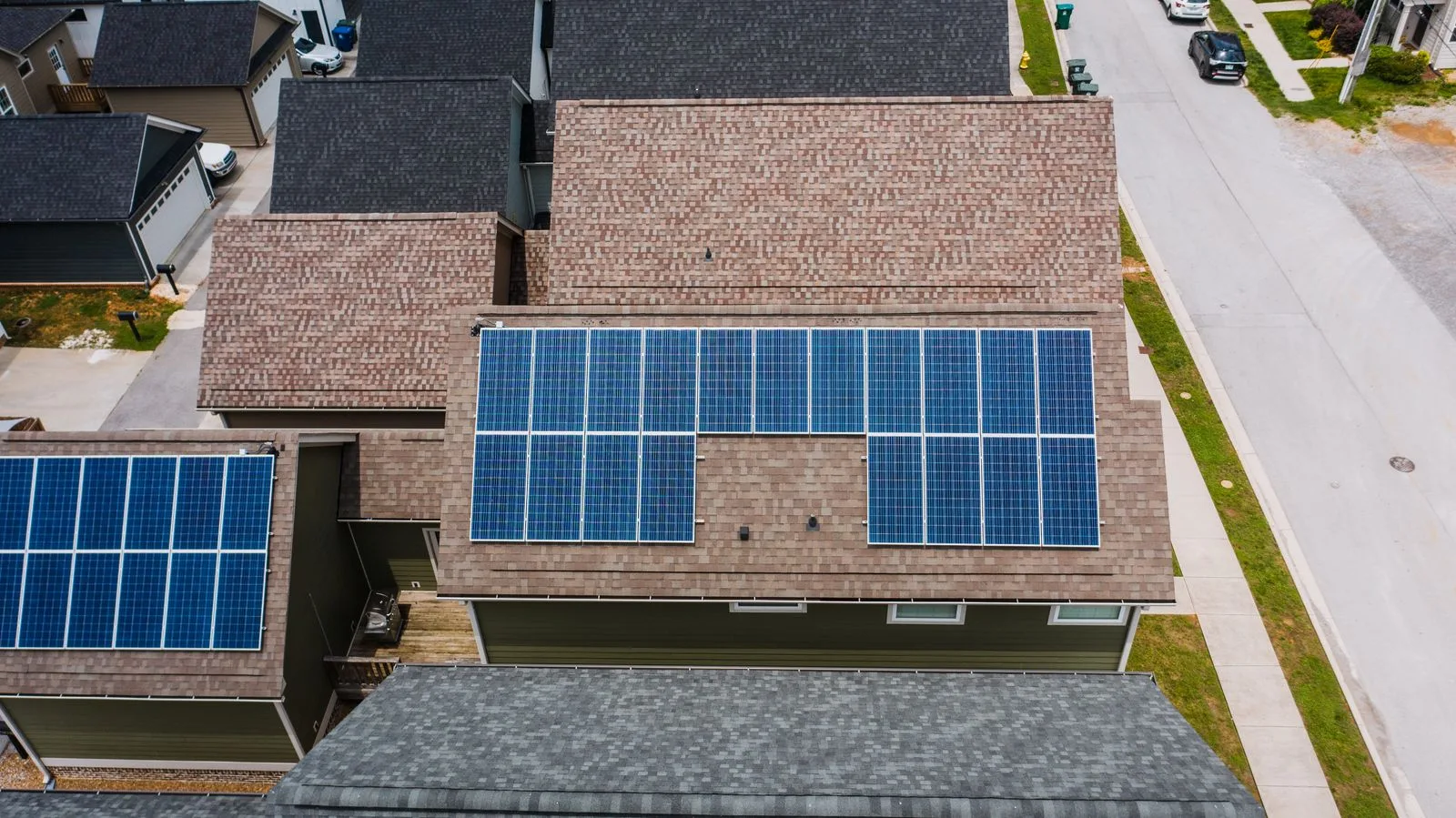 An aerial view of solar panels on the shingled roofs of suburban houses