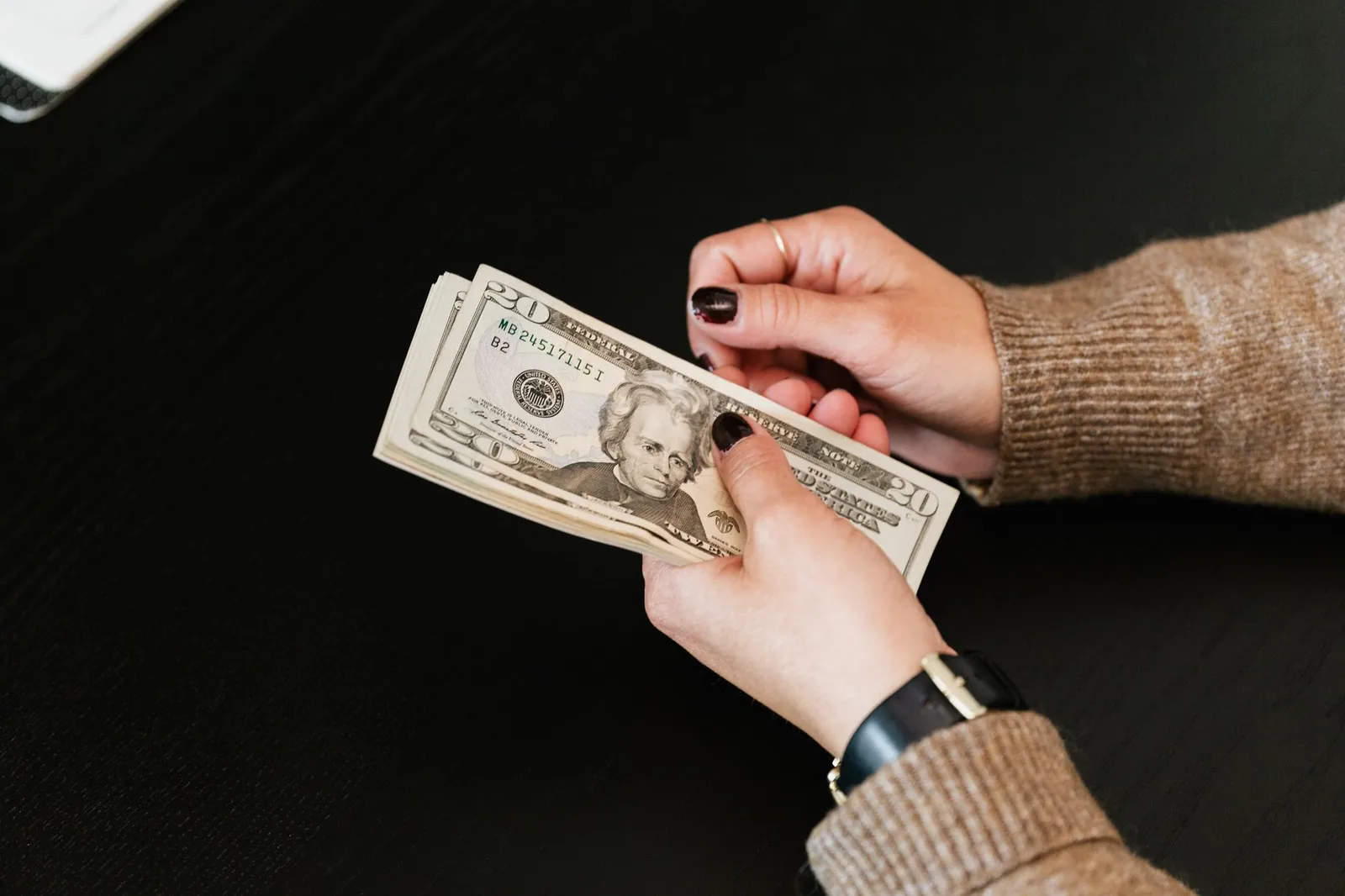 Hands counting a stack of twenty dollar bills on a dark table