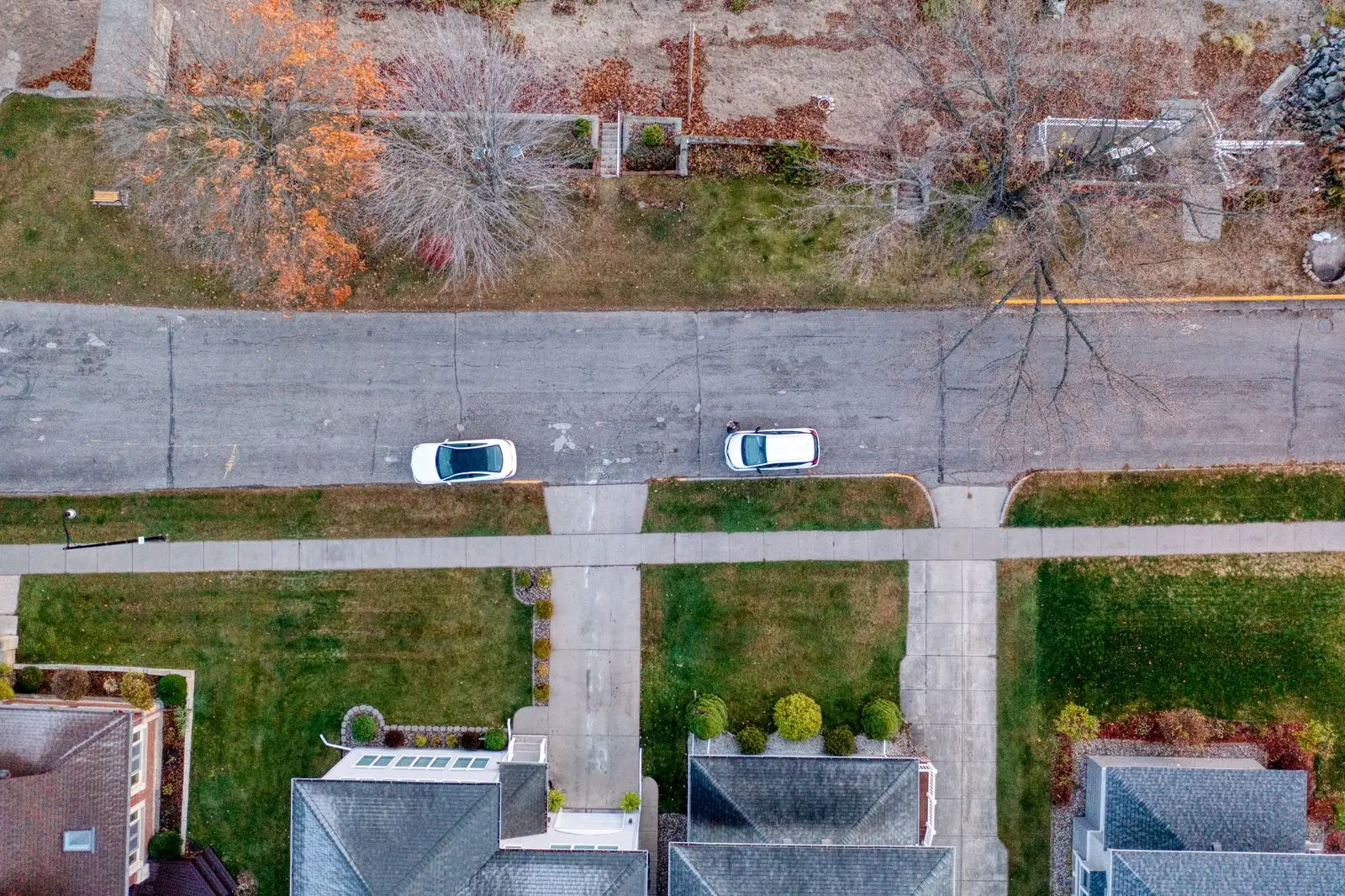 Overhead view of a quiet suburban street with two cars parked at the curb in front of houses