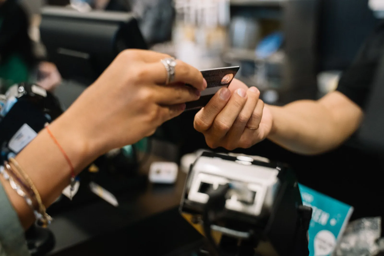 Customer handing a bank card to a cashier across a store checkout counter