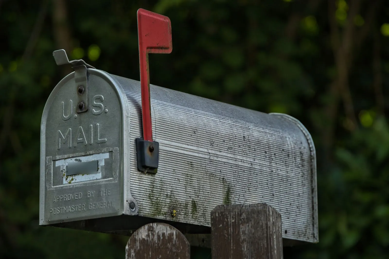 Weathered metal U.S. mailbox with its red flag raised on a wooden post