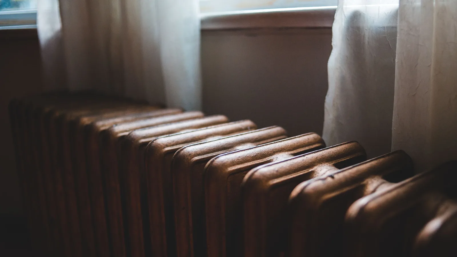 Old cast iron radiator beneath a curtained window in a quiet room